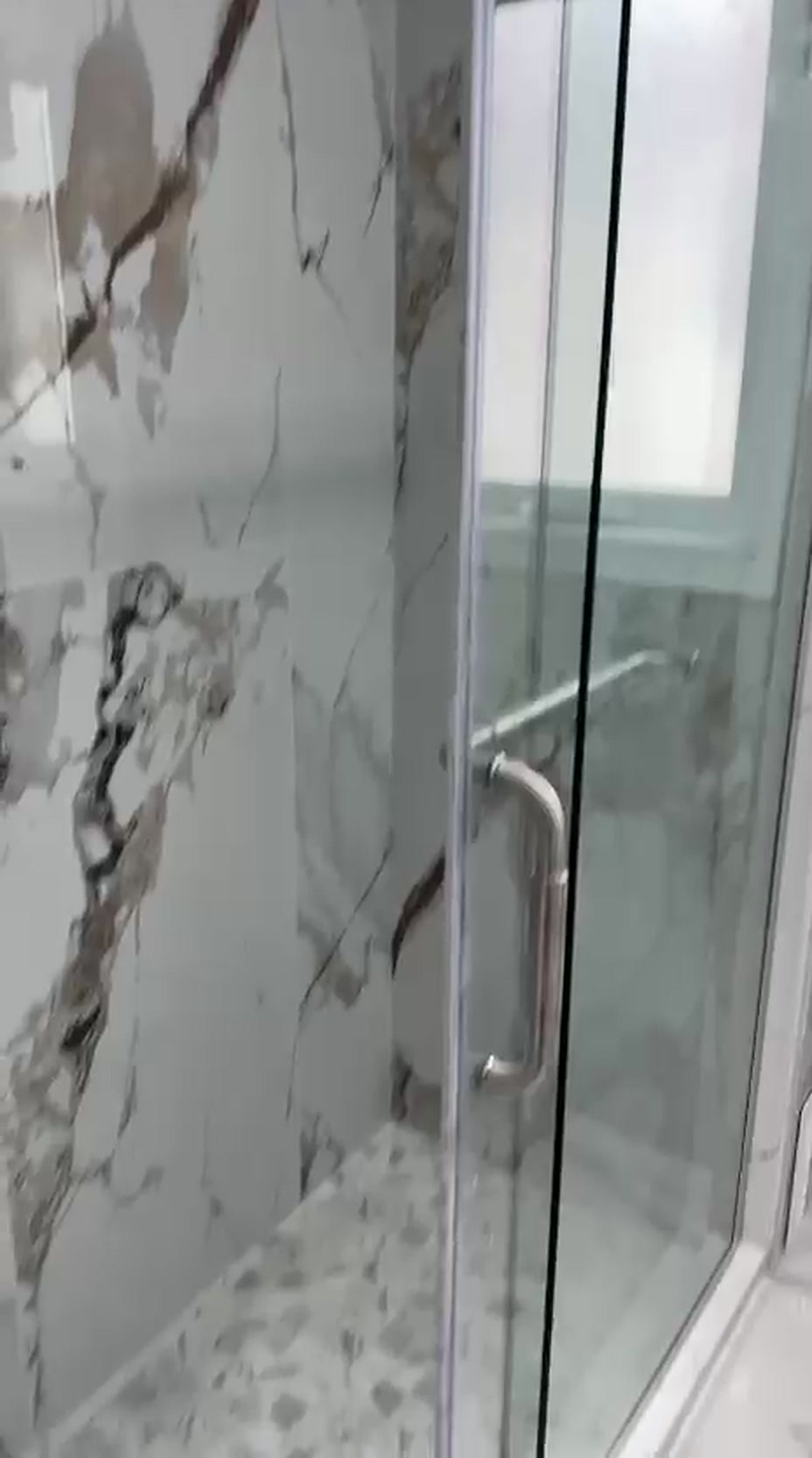 Completed Toronto ensuite renovation with book-matched marble-look porcelain walls and a frameless glass shower door